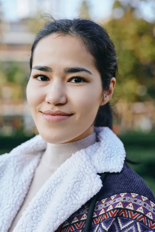 Smiling woman in an outdoor setting wearing a shearling jacket with a patterned trim, casual fashion style and warm outerwear suitable for autumn days and cool weather
