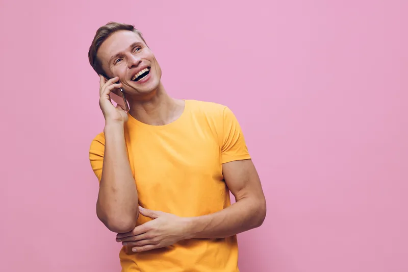 Smiling woman wearing yellow t-shirt talking on mobile phone looking happy cheerful isolated on pink studio background. People lifestyle concept