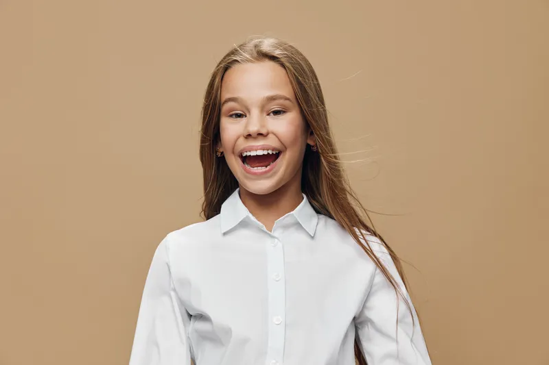 Girl smiling with long hair and white shirt standing on beige background. Child happy and cheerful expression for childhood, youth and casual style portrait.