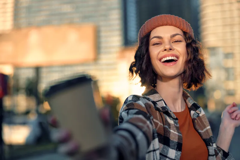Woman with smile taking a selfie in an urban street, candid and joyful portrait capturing authenticity, golden hour glow, candid lifestyle, mindful living and emotional storytelling.