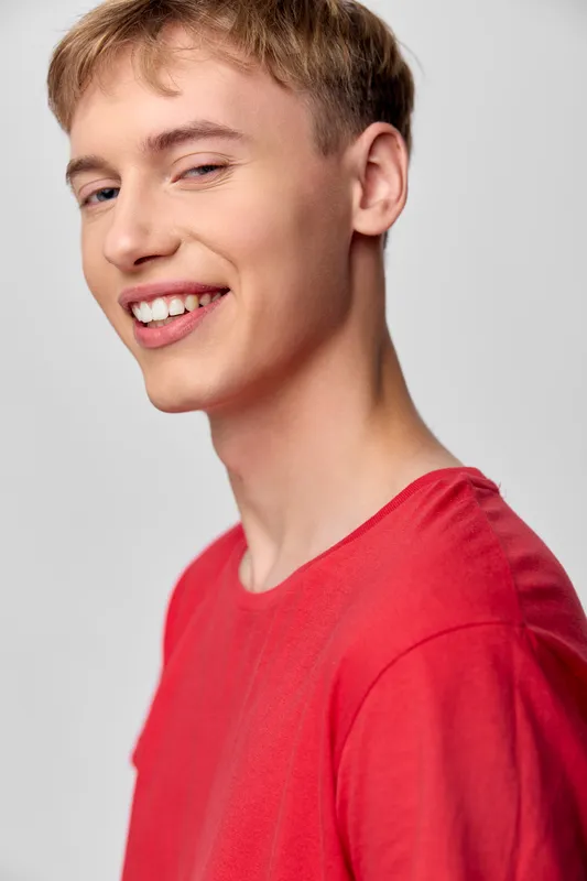 Smiling man in a red shirt in a casual studio setup, showcasing friendly confidence and approachable vibe for lifestyle and fashion imagery