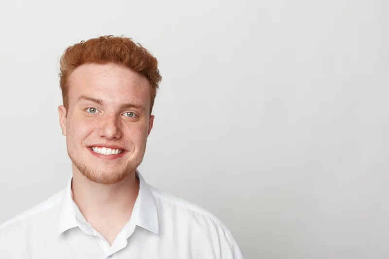 Smiling young man with red hair and freckles wears white shirt, looking at camera on light background. Concept of happiness, youth, casual style, and natural portrait photography.