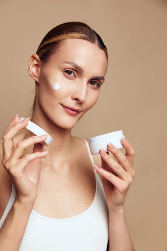 Cheerful woman applying cream, skincare routine in progress, soft lighting, close up on face, natural tones, gentle texture on skin, calm and confident mood