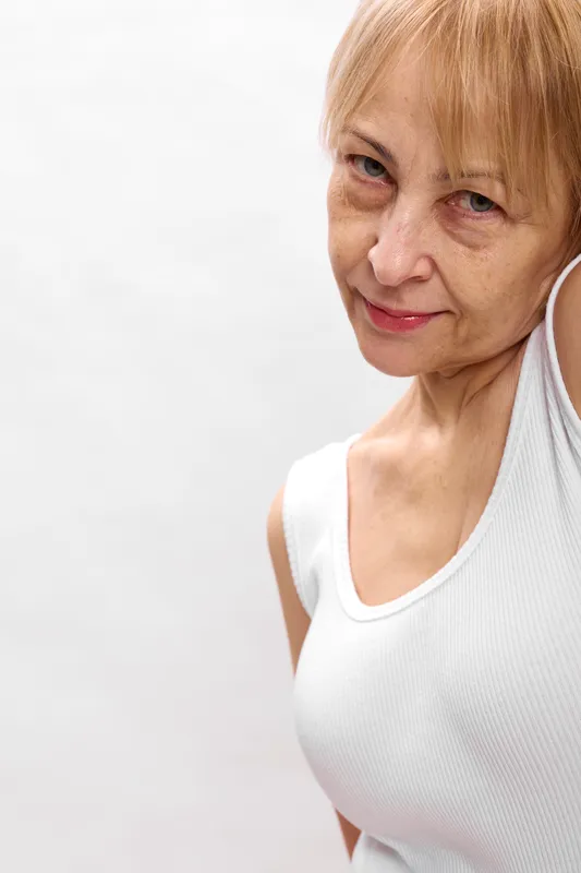 Woman senior portrait face smile eyes indoor closeup white blouse, gentle expression, natural light, plain studio background, soft skin texture, calm mood, copy space