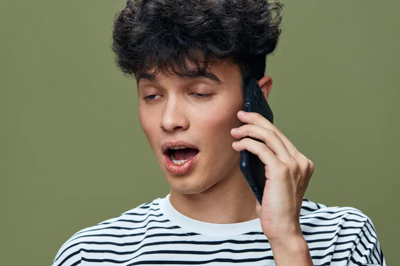 young man talking phone striped shirt casual hairstyle green background expressive communication smartphone