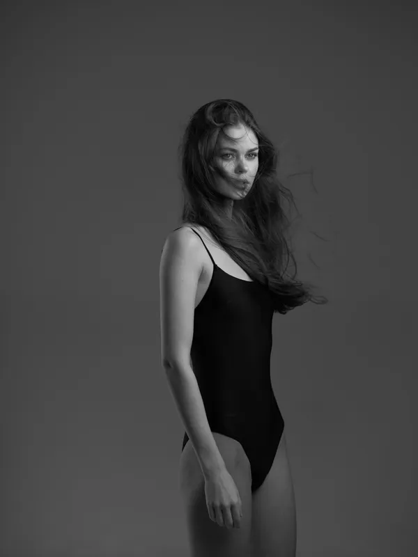 Black and white portrait of a slender woman in a simple black swimsuit with flowing hair in studio light