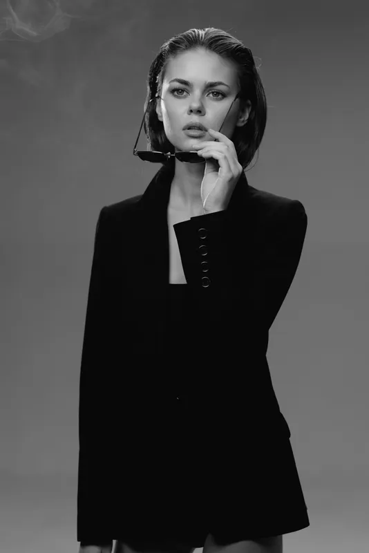Black and white portrait of a confident woman in stylish black jacket smoking a cigarette with calm expression and smoky background.