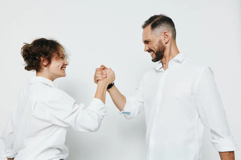 A professional man and colleague share a confident fist bump against a simple colored background, conveying teamwork, success, and positive emotion in a modern business scene.