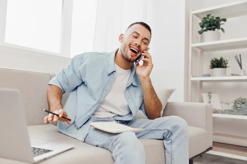 Cheerful man talking on phone while making notes, showcasing a modern workspace and a joyful atmosphere, ideal for business and lifestyle projects.