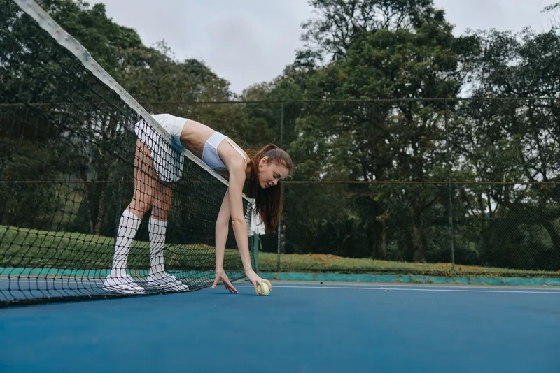 Young female tennis player in white sportswear preparing to serve on a green outdoor court, showcasing focus and determination in a vibrant sports environment