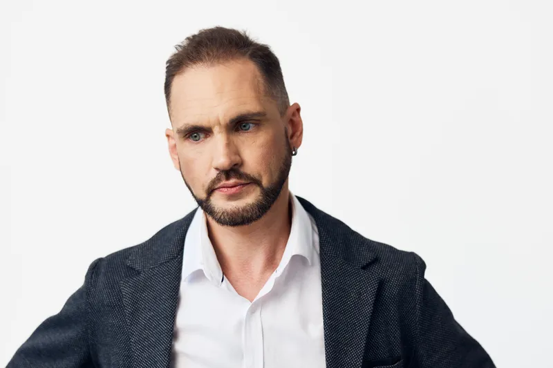 A professional man in business attire stands against an isolated colored backdrop, conveying confident emotion and focus. The subject projects leadership, determination, and calm poise for corporate