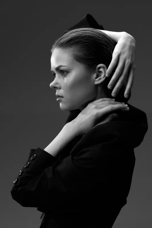 Black and white portrait of a contemplative woman with hands near face, showing emotion and elegance in studio lighting.