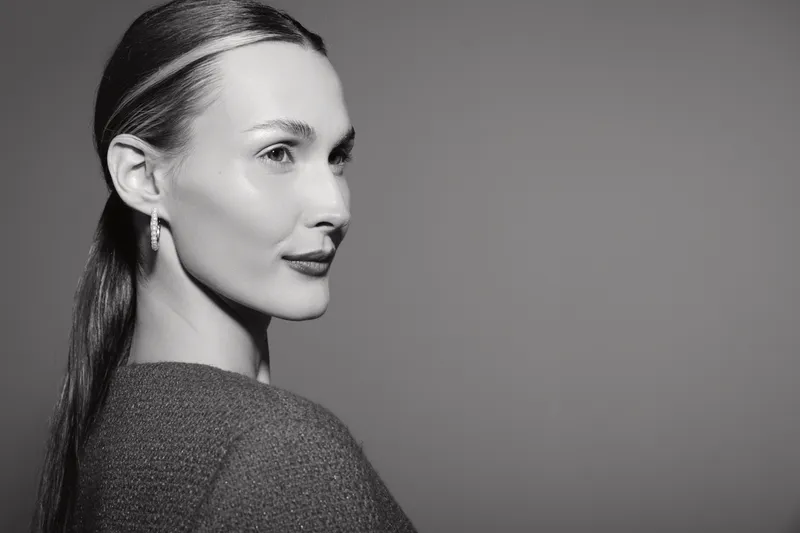 Profile of a fair skinned caucasian woman with slicked back hair wearing earrings and a knitted top looking away on grey background. Concept of elegance, fashion, and beauty.