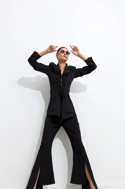Fashion woman posing in stylish black outfit with sunglasses against white background, showcasing modern fashion and confident attitude in minimalist setting.