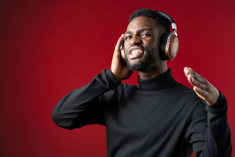 Happy young man enjoying music with headphones against a vibrant red background, expressing joy and energy, perfect for music and lifestyle themes