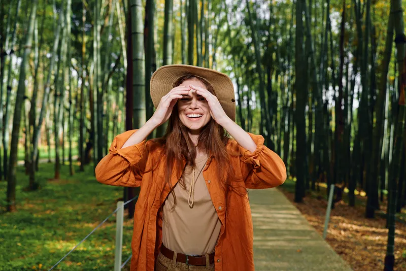 woman hat bamboo forest smile walkway, redhead traveler wearing straw hat and casual outfit on wooden boardwalk through bamboo grove, portrait of happy lifestyle and nature escape.