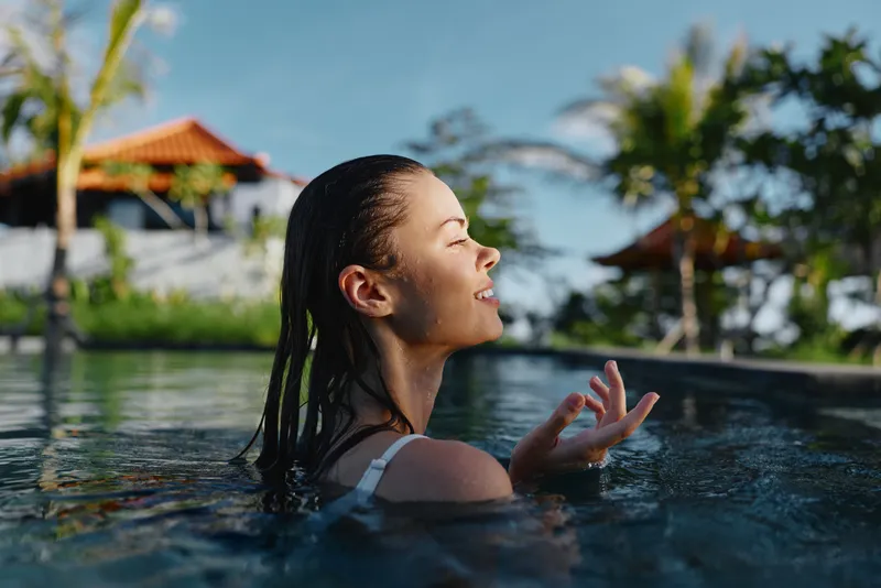 Relaxed woman enjoying a sunny pool moment, soaking in warm breeze, water sparkles, tropical outdoor setting, carefree lifestyle and peaceful refreshment.