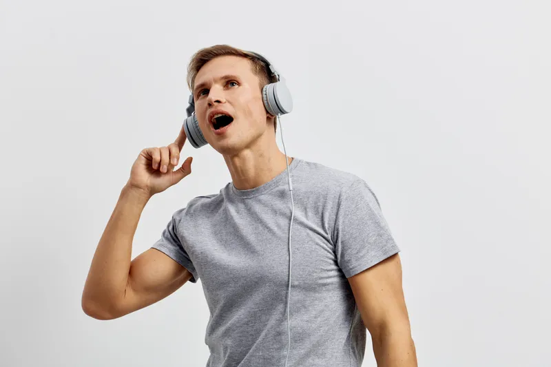 Young man with headphones listening to music, expressing joy and excitement, wearing casual gray t-shirt, isolated on white background, studio portrait, lifestyle concept.