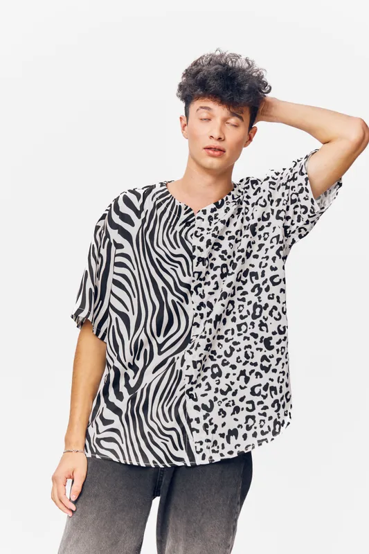 young man wearing a black and white animal print shirt with zebra and leopard patterns, casual pose, curly hair, neutral background, modern fashion style