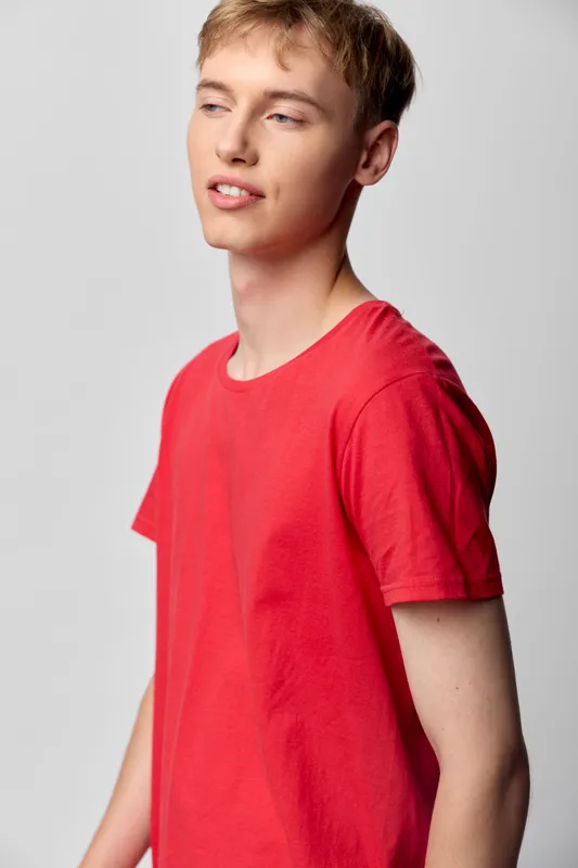 Young man in a red t shirt stands casually against a light background, relaxed expression, clean style, everyday fashion, relaxed pose, studio shot, minimalistic mood
