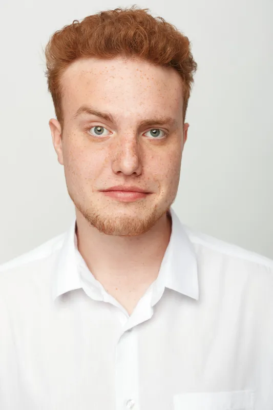 Portrait of a young redhead man with freckles wearing a white shirt looking at camera on white background. Concept of natural beauty, confidence, and casual style.