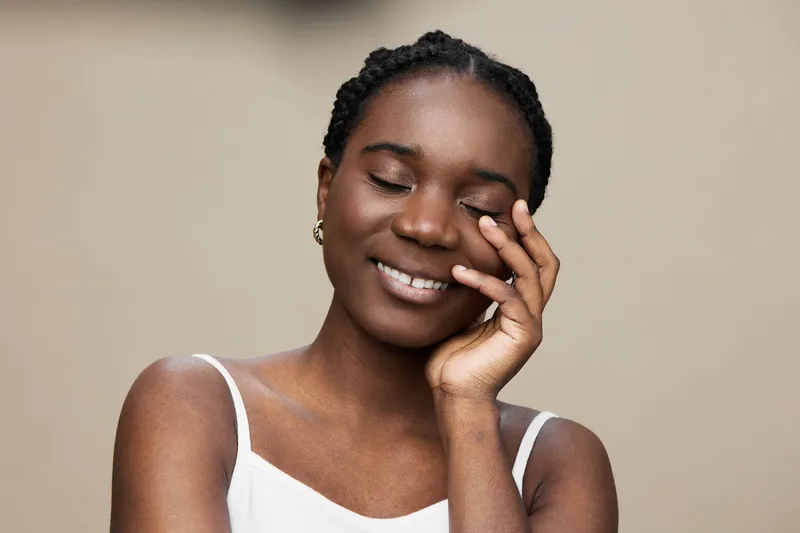 Joyful young woman with braids, expressing happiness and serenity, wearing a white top, with a neutral background emphasizing her warm smile and natural beauty
