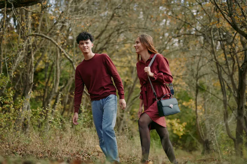 Candid portrait of a young couple walking through autumn woods, natural expressions and relaxed posture convey authentic, honest connection amid soft golden foliage.