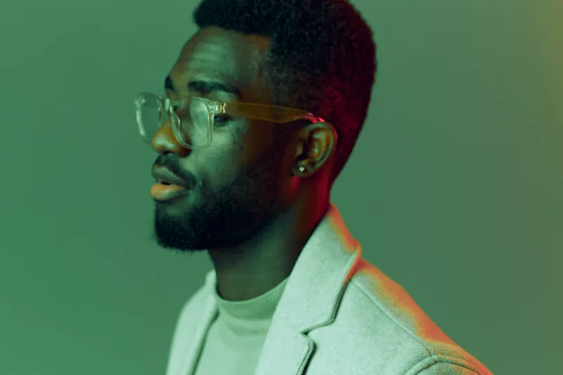 Stylish African man in glasses with a neutral expression against a vibrant green background, showcasing modern fashion and individuality in a creative portrait