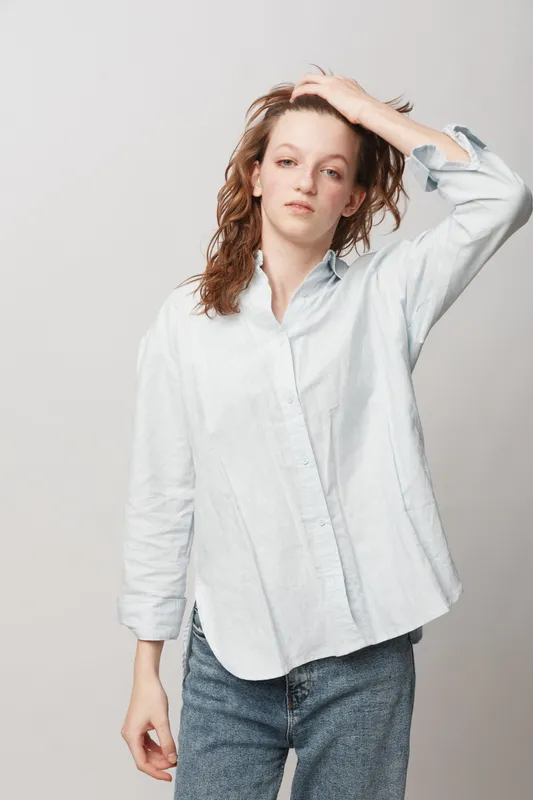 Young woman with wet hair wearing a white shirt and jeans stands against a plain background, touching her head. Concept of casual style, natural beauty, and relaxed mood.