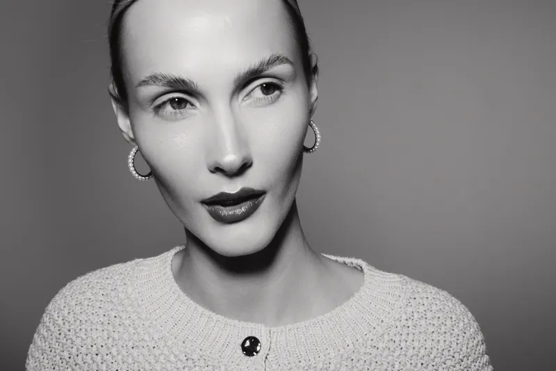 Closeup portrait of a young white woman with pale skin wearing hoop earrings and a knitted sweater. Studio shot with soft lighting and neutral background.
