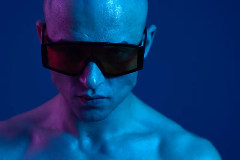 Stylish man with sunglasses showcasing a unique blend of blue and purple tones, exuding confidence and modernity in a vibrant background.