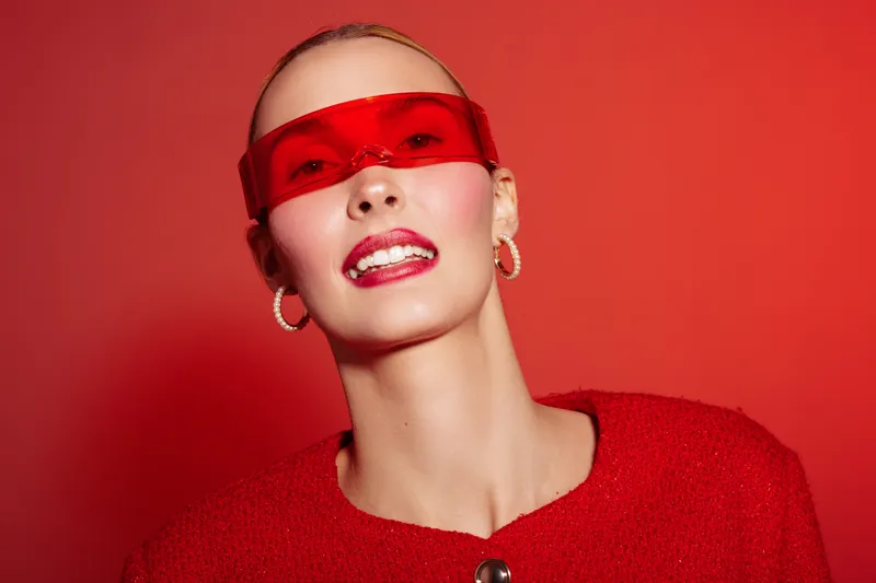 Portrait of a confident woman wearing red sunglasses and a red sweater against a red background. Fashion concept with bold colors and modern accessories in studio lighting.