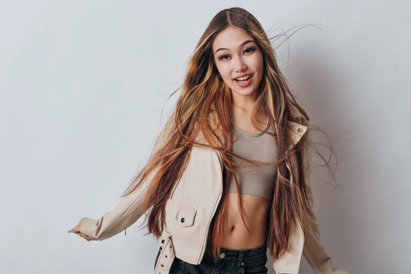 Young woman with long hair posing in casual beige jacket and crop top on light background. Smile, fashion style, beauty and confident female model portrait in studio shot.