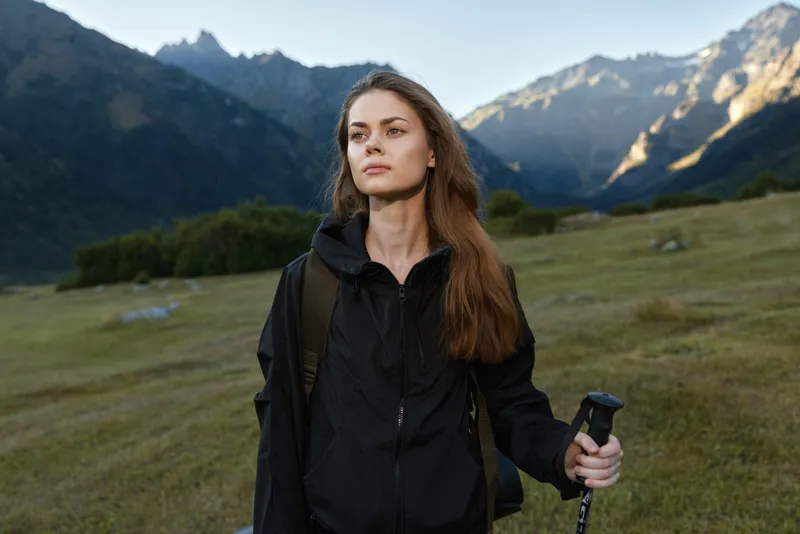 A thoughtful young hiker stands in a rugged mountain landscape, gripping a trekking pole and gazing into the distance, exuding adventure, focus, and determination in a pristine alpine setting.