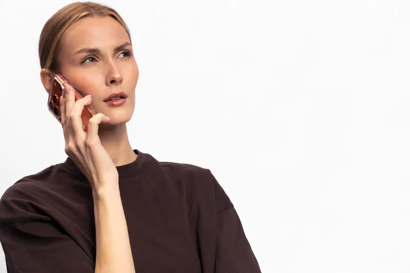 Young woman in dark shirt talking on smartphone, looking thoughtful isolated on white. Concept of communication, technology, and modern lifestyle in casual wear.