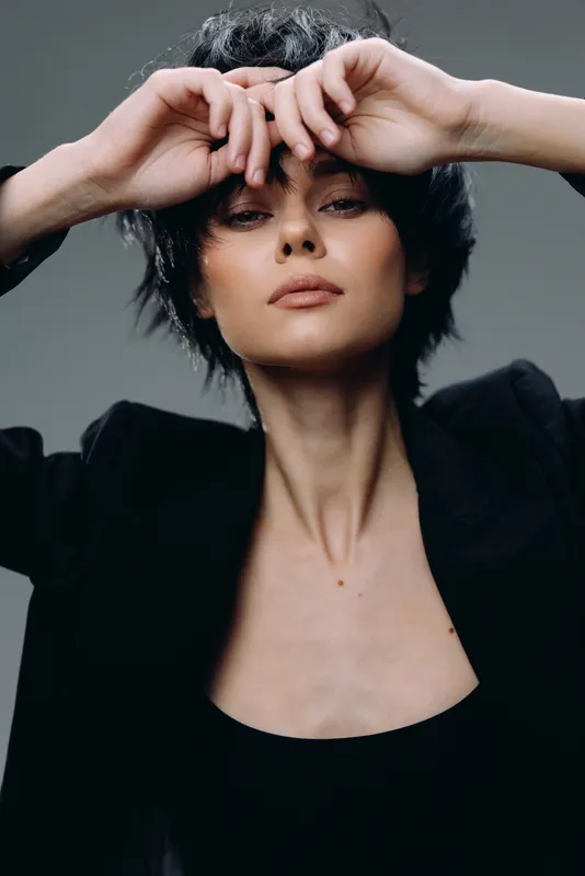Elegant woman with short dark hair posing in black outfit, showcasing confidence and style in a minimalist studio setting.