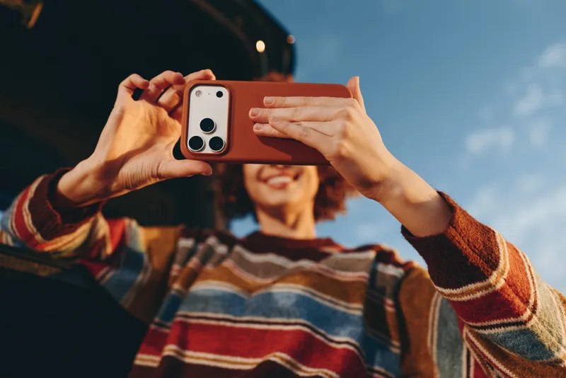 Woman lifestyle outdoors, hands holding smartphone, taking photo with blurred background, closeup upperbody, casual sweater, daylight atmosphere, relaxed playful mood, natural colors