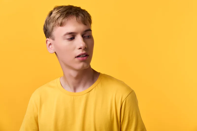 Young man in a yellow shirt stands before a solid yellow background with a relaxed pose, soft lighting, and a modern casual style suitable for fashion stock, lifestyle imagery, and bright mood visuals