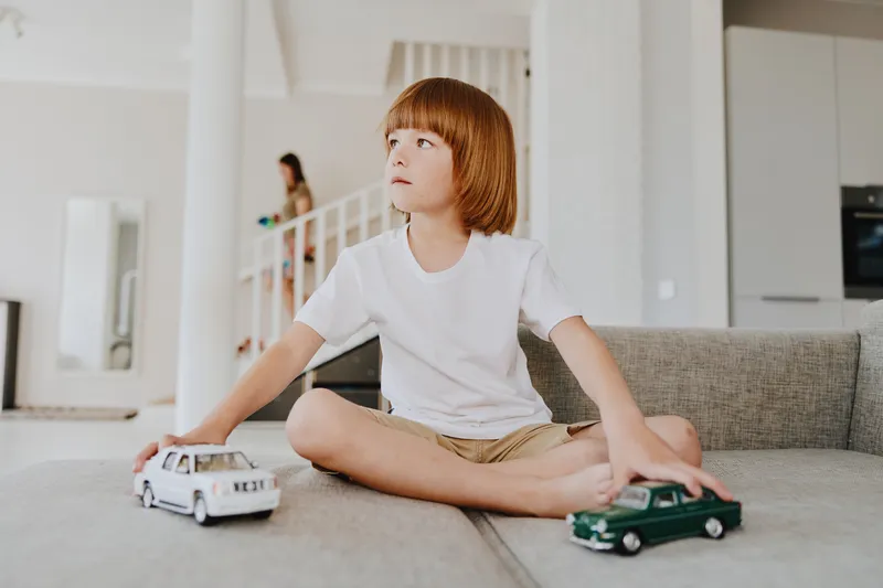 Thoughtful boy playing with toy cars in a bright and modern living room, showcasing creativity and imagination while enjoying a relaxed afternoon.