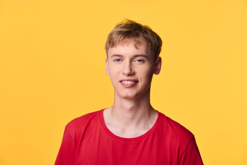 Smiling young man wearing a red shirt against a bright yellow backdrop, relaxed and approachable for lifestyle, fashion, corporate branding, or marketing concepts.