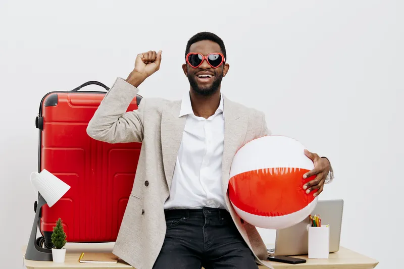 Cheerful smiling man with sunglasses holding beach ball and standing in front of travel luggage isolated on white background. Vacation, summer, leisure, holiday, fun, travel accessories