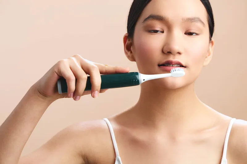 asian woman brushes her teeth with an electric toothbrush in a clean bathroom, focused expression and fresh mood, highlighting daily hygiene and personal care in a modern setting.