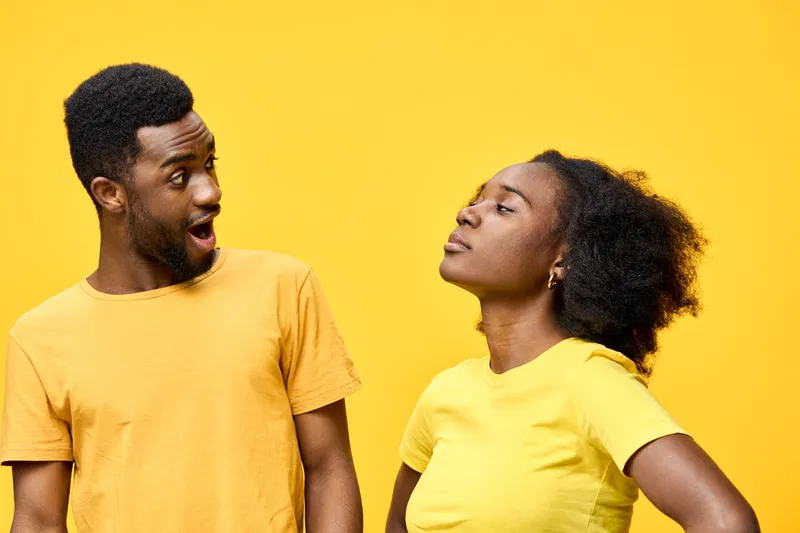 Young African couple expressing playful emotions with vibrant yellow background, showcasing trendy casual attire and joy in their poses