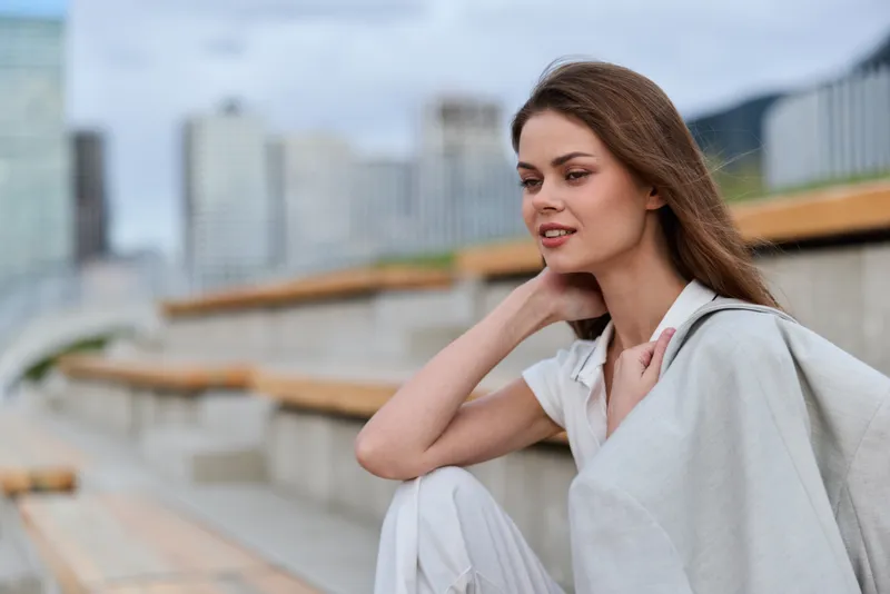Young woman in white casual outfit outdoors with thoughtful expression in urban setting, soft natural colors, spring fashion and lifestyle concept