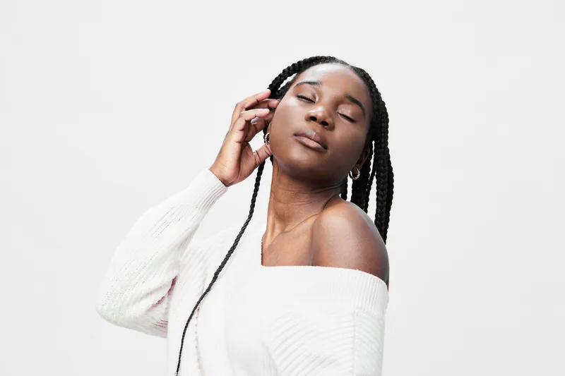 Beautiful Black woman with braided hair in a cozy white sweater, exuding confidence and serenity in a minimalist studio setting