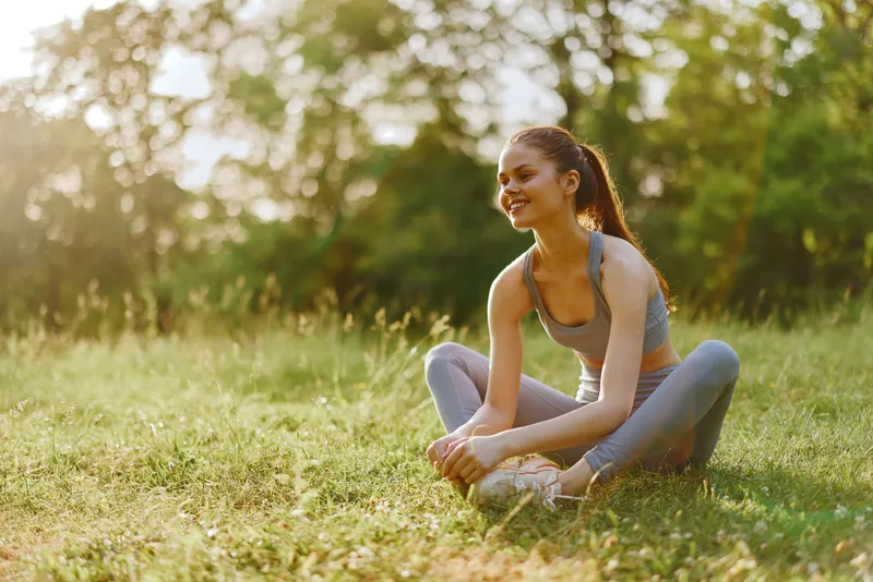 Young athletic woman stretching outdoors in a green park, illustrating healthy lifestyle, fitness, and outdoor exercise in summer