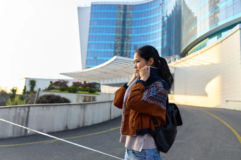 Woman street backpack jacket city outdoor urban phone casual architecture talking on her cellphone beside modern buildings during daylight, showcasing travel, communication and city life