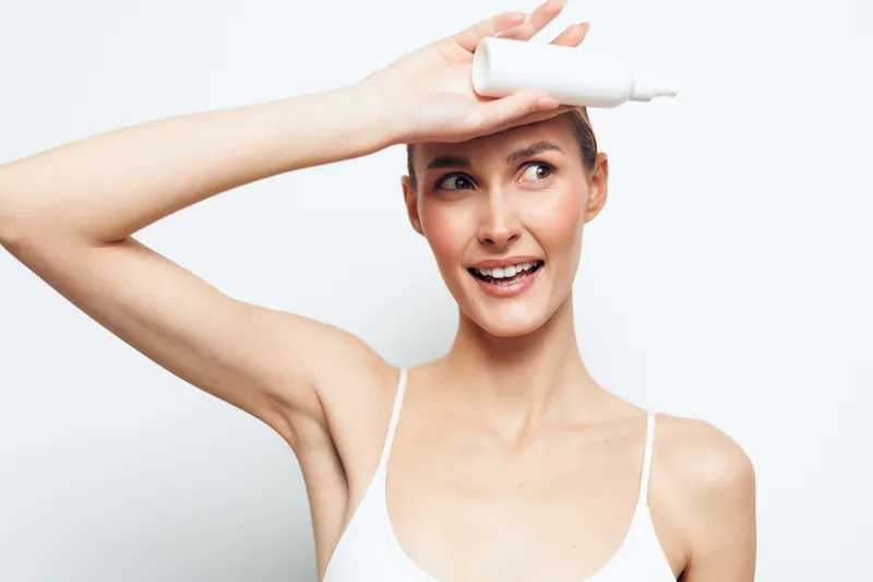Happy woman portrait in white studio, smiling with arms raised while adjusting hair and glasses, skincare beauty routine, soft light, minimal background, relaxed pose
