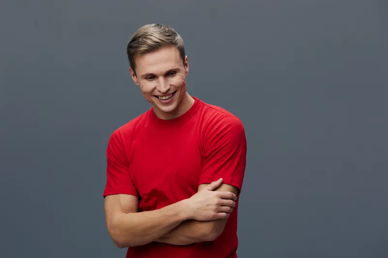 Smiling young man wearing bright red t-shirt on plain gray background studio portrait. Happy, cheerful, relaxed, casual, fashion, portrait, positive emotion, people lifestyle concept