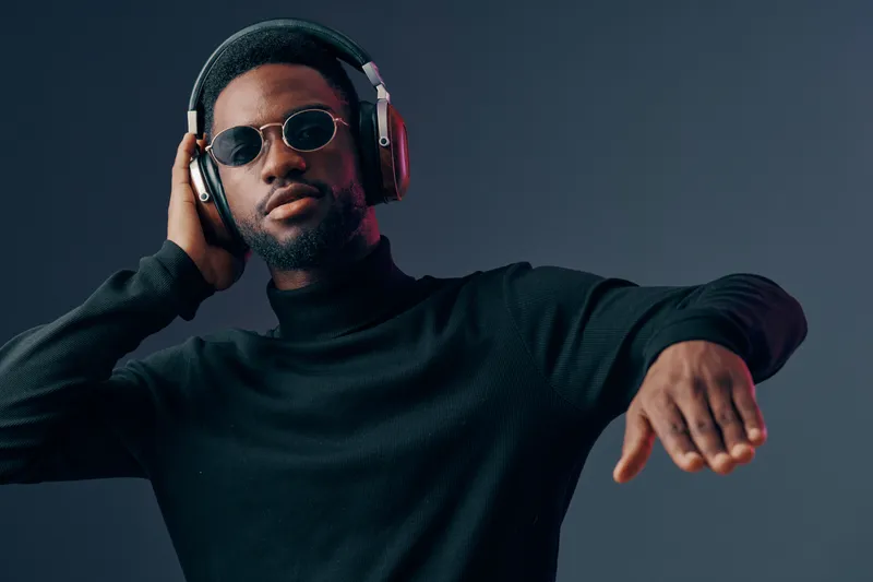 Stylish African man with headphones enjoying music in a modern setting, dressed in a black turtleneck and sunglasses expressing joy